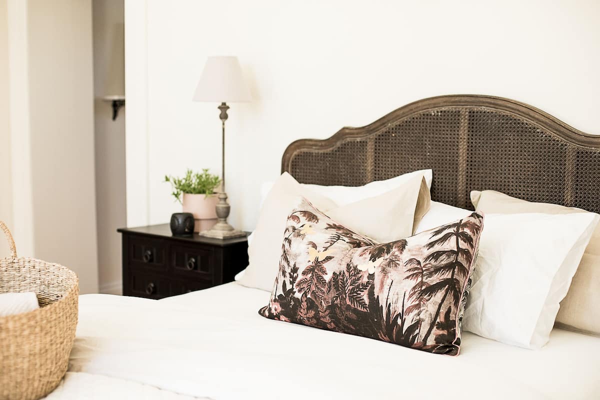 A neatly made bed with a woven headboard, a bedside table with a lamp, and a basket.