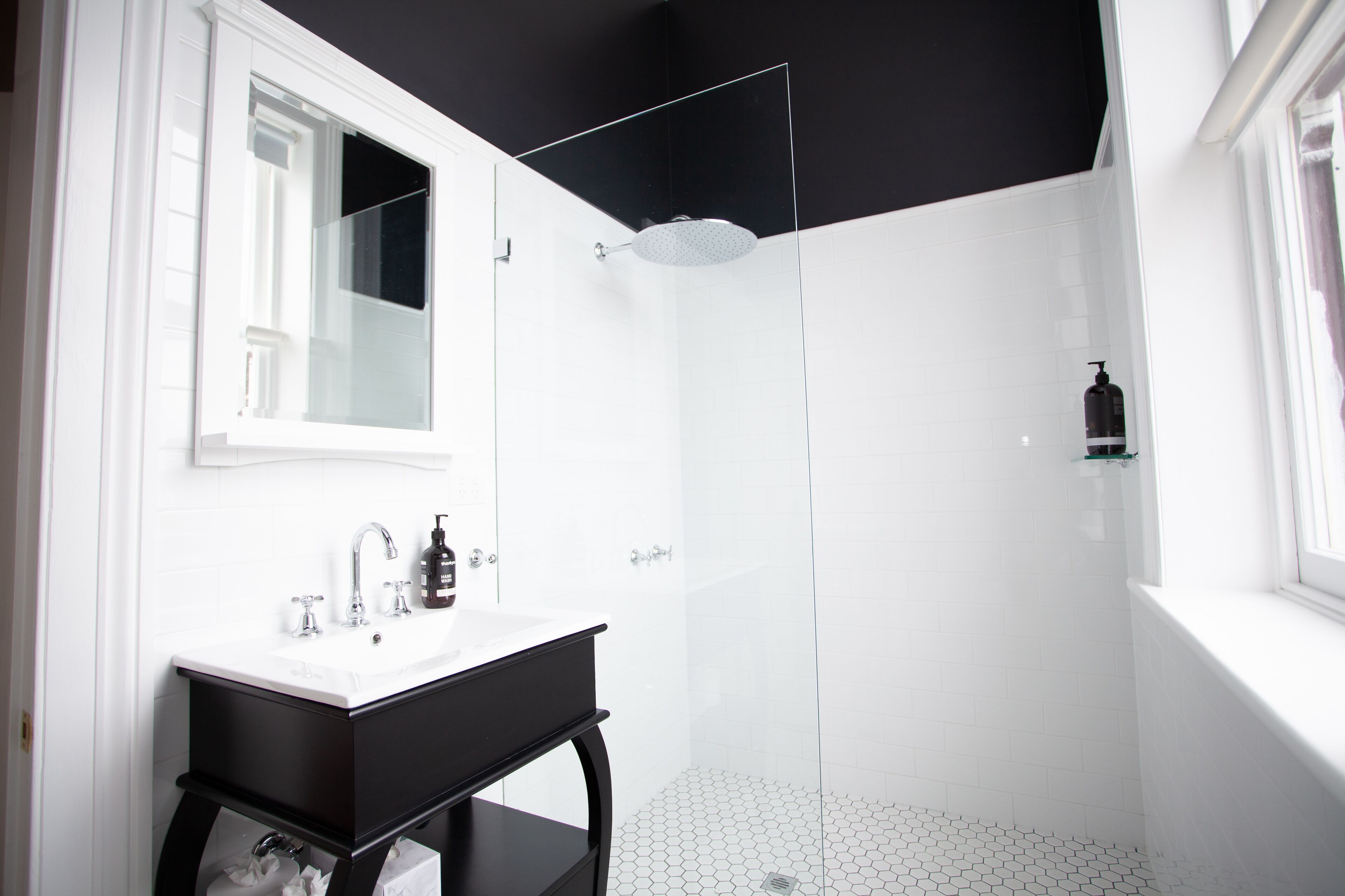 A bathroom with a white sink, black vanity, and a glass shower enclosure.
