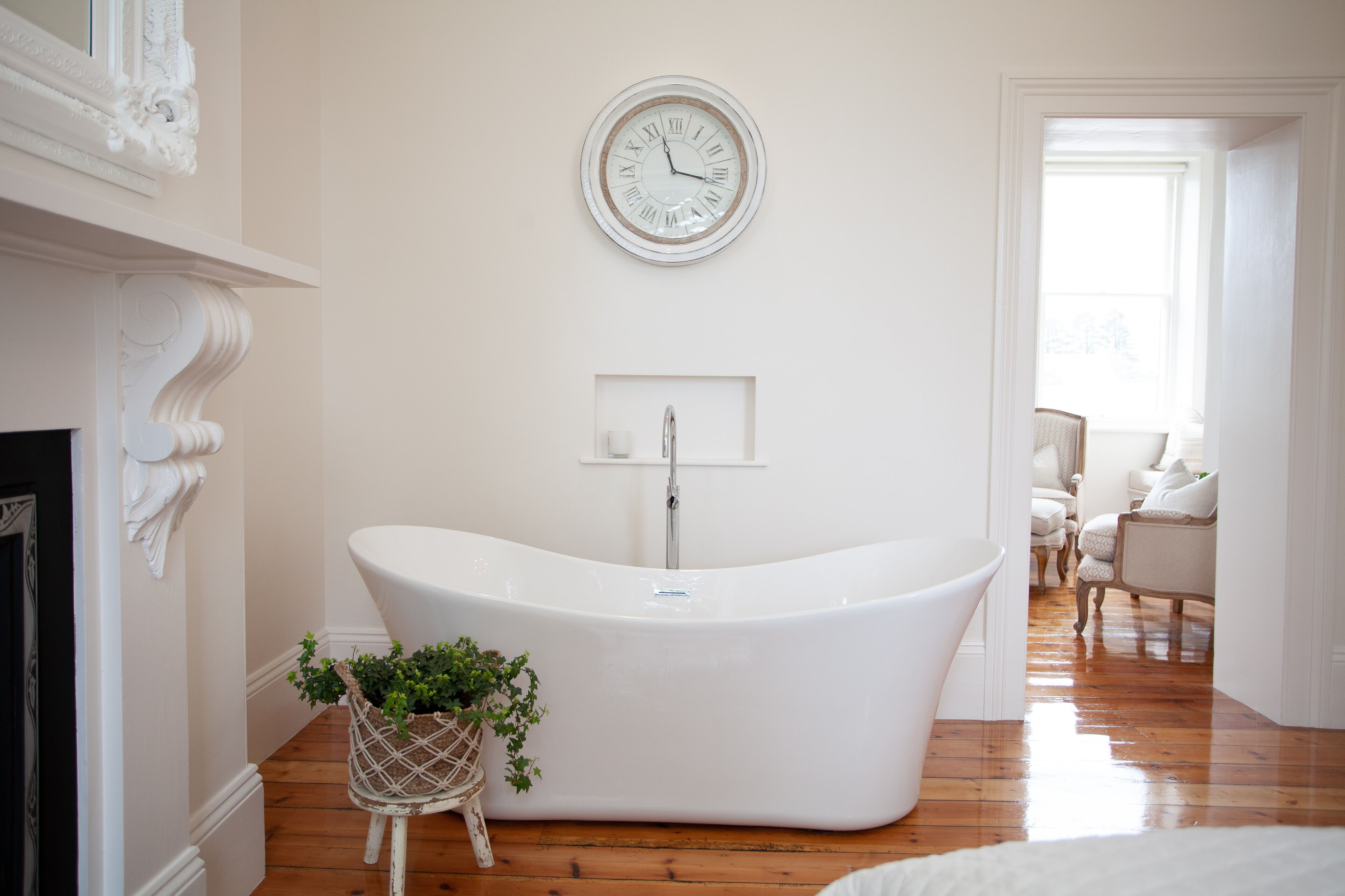 A modern bathroom with a freestanding bathtub, a wall-mounted clock, and a small plant beside the tub.