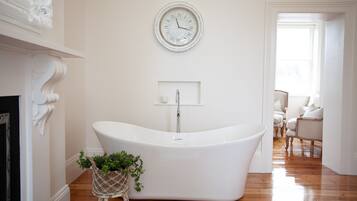 A modern bathroom with a freestanding bathtub, a wall-mounted clock, and a small plant beside the tub.