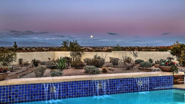 Una piscina con baldosas azules, rodeada de plantas del desierto y una vista de la ciudad al atardecer.