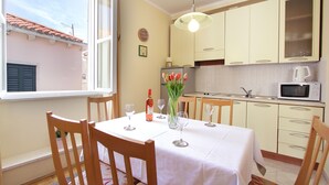Un comedor con una mesa preparada para cuatro, una cocina con microondas y lavamanos, y una ventana con vistas a un edificio de techo rojo.