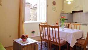 Un comedor con una mesa dispuesta para dos, sillas, un frutero y una ventana con vista a un edificio de piedra.