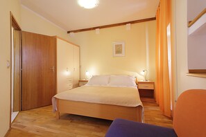 A bedroom with a wooden bed, two bedside tables with lamps, a wooden wardrobe, and a window with orange curtains.
