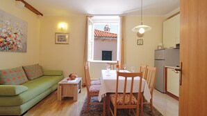 Un espacio habitable compacto con comedor, un sofá verde, una mesita con frutero y vistas a un edificio desde la ventana.
