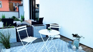 An outdoor patio with white furniture, star-patterned rug, and potted plants.