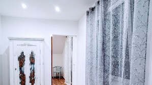 A room with wooden flooring, a white cabinet with decorative panels, a wooden bench, and sheer curtains with a floral pattern.
