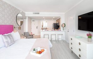 Una habitación de hotel moderna con cama, bandeja de desayuno, televisor, zona de cocina y mesa de comedor.