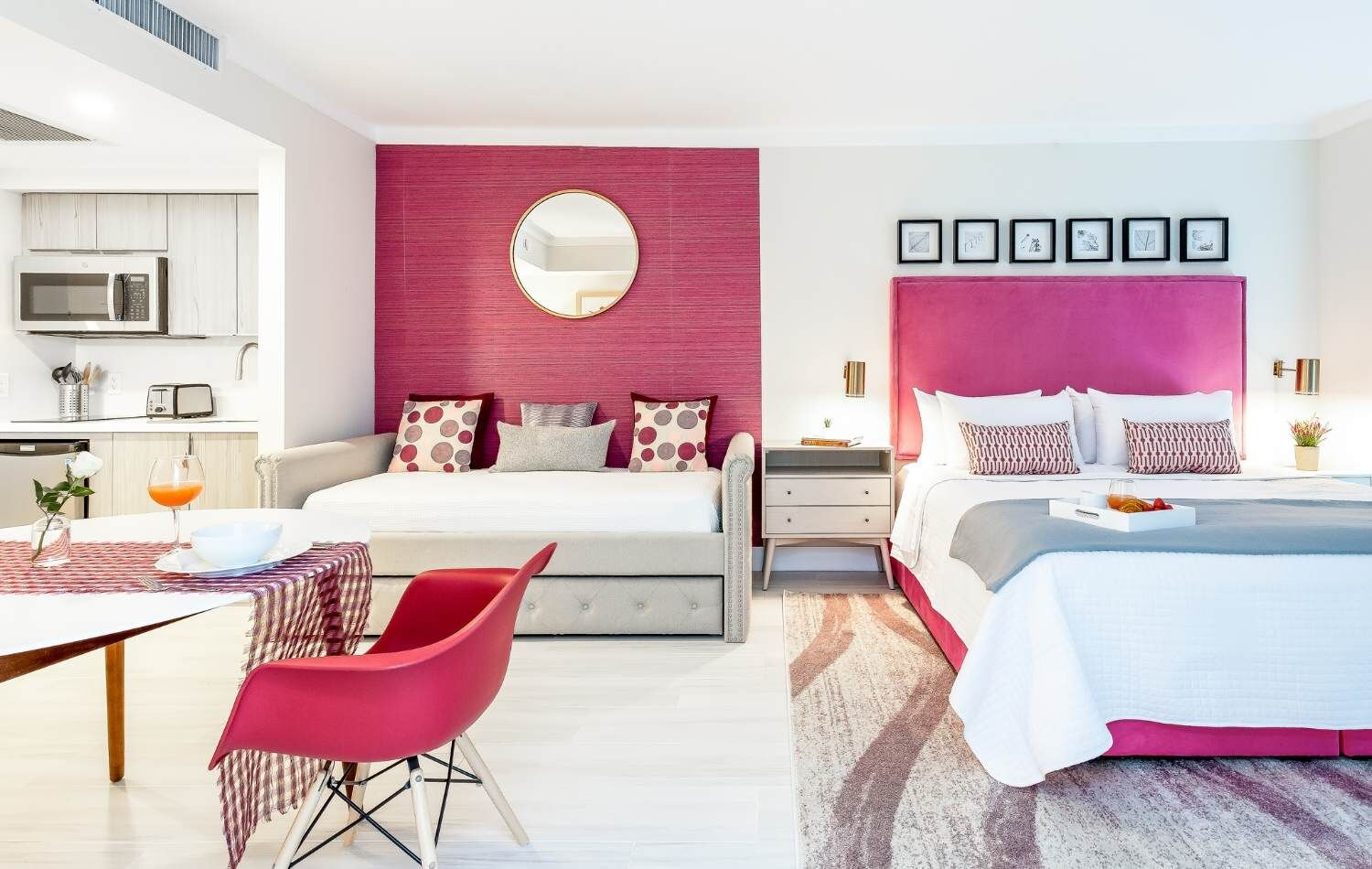 Ein modernes Schlafzimmer mit einem großen Bett, einem Nachttisch, einem roten Sessel und einem Essbereich mit Tisch und Stühlen.