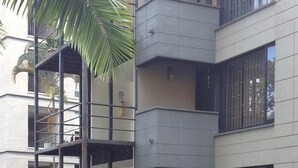 A multi-story building with balconies, surrounded by lush greenery and a brick pathway.