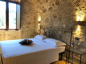 Ein Schlafzimmer mit einer Steinsandsteinwand, einem Bett mit weißen Leinentüchern und zwei Wandleuchten.