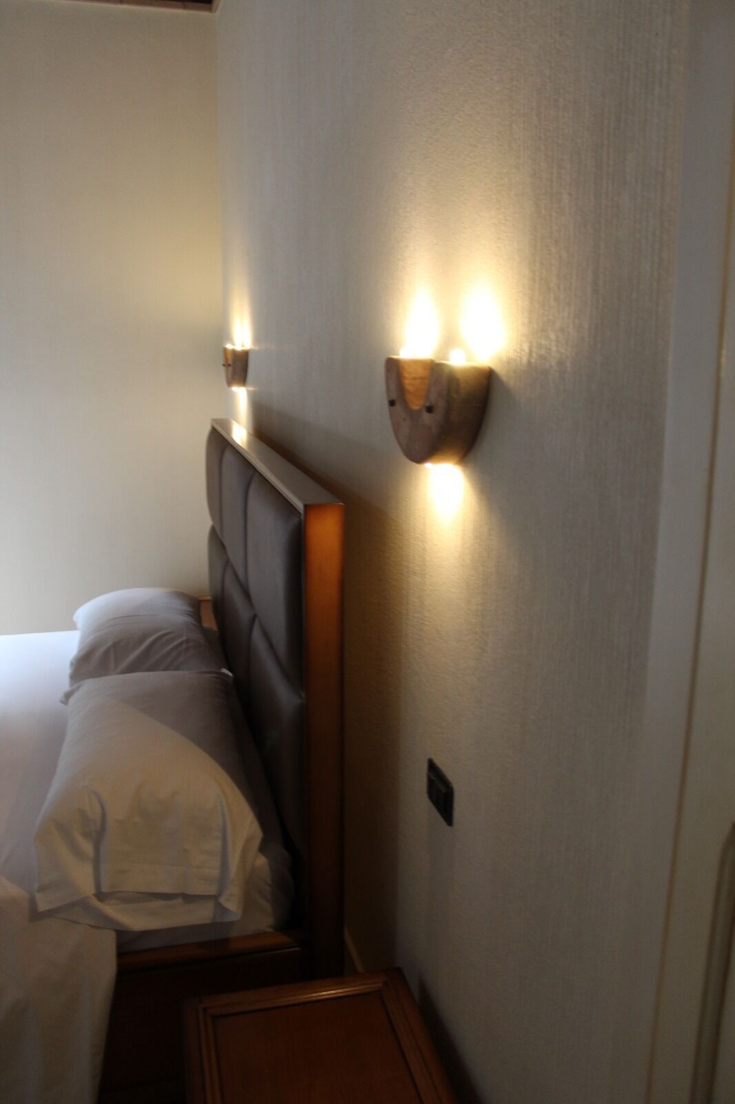 A hotel room with a bed, a headboard, and a wall-mounted light fixture.