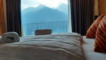 Une chambre d’hôtel avec un lit, une vue sur les montagnes par une grande fenêtre et une balustrade de balcon.