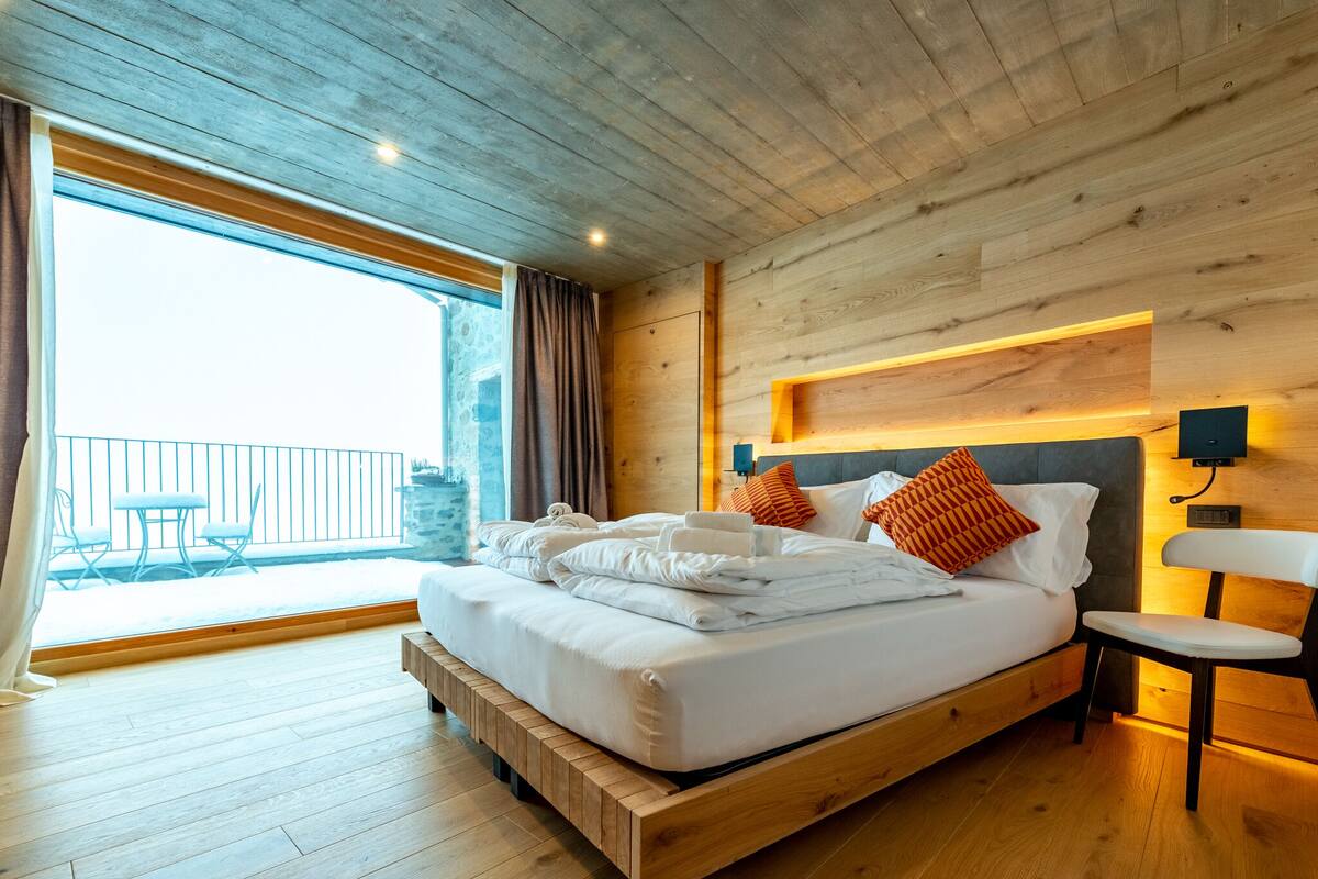 A spacious bedroom with a large bed, wooden ceiling, and a balcony with outdoor seating.