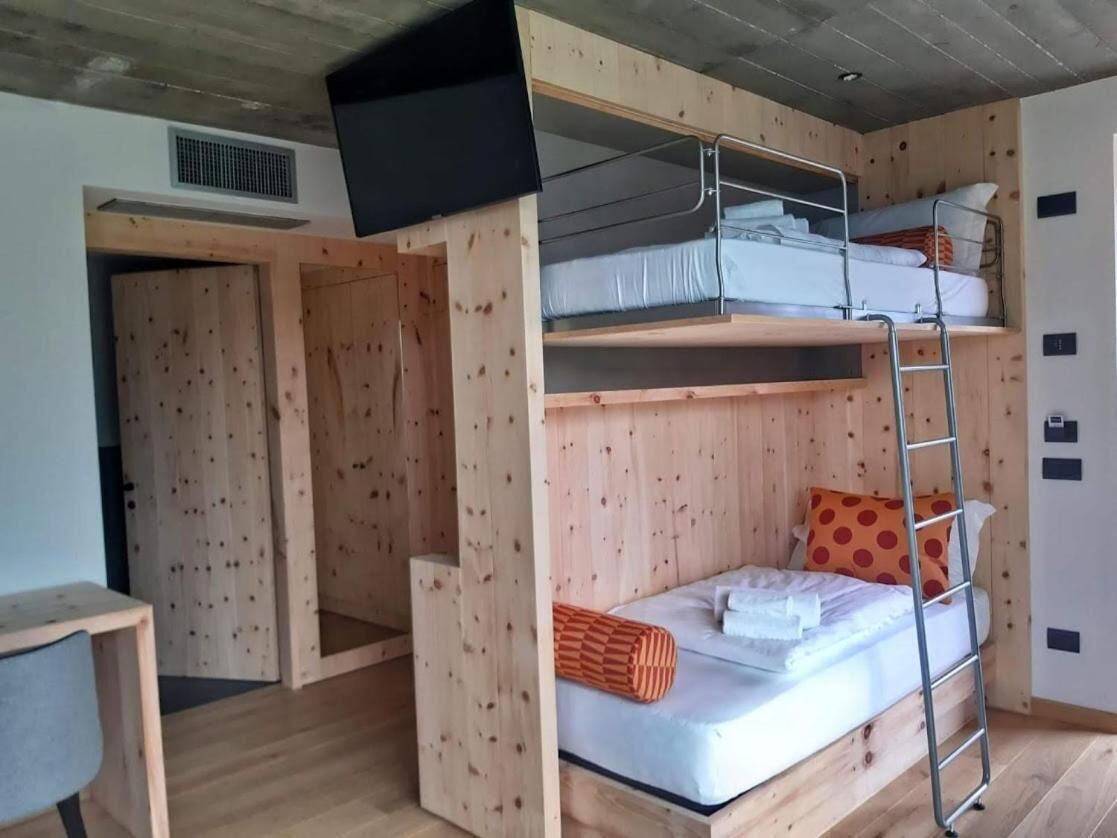 A bunk bed room with a TV mounted on the wall, a wooden door, and a small desk.