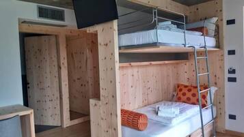 A bunk bed room with a TV mounted on the wall, a wooden door, and a small desk.