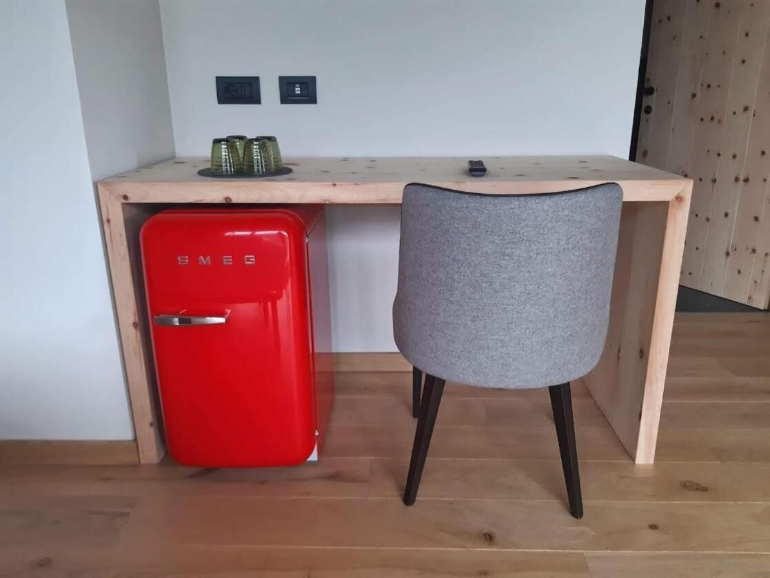 Een kleine werkruimte met een rode Smeg-koelkast, een grijze stoel en een houten bureau.