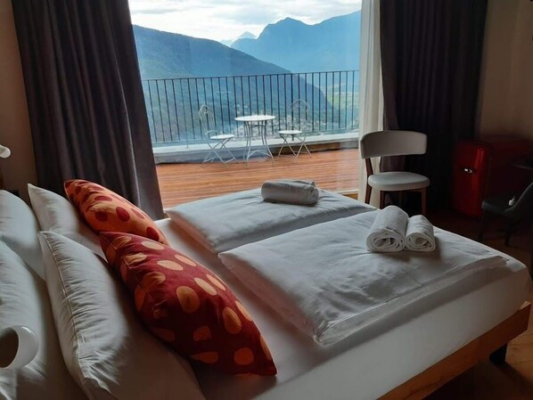 Ein Hotelzimmer mit Bett, Kissen, einem kleinen Tisch und Bergblick vom Balkon.