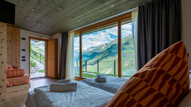 A bedroom with a large window offering a mountain view, a bed with white linens, and a wooden bench with cushions.