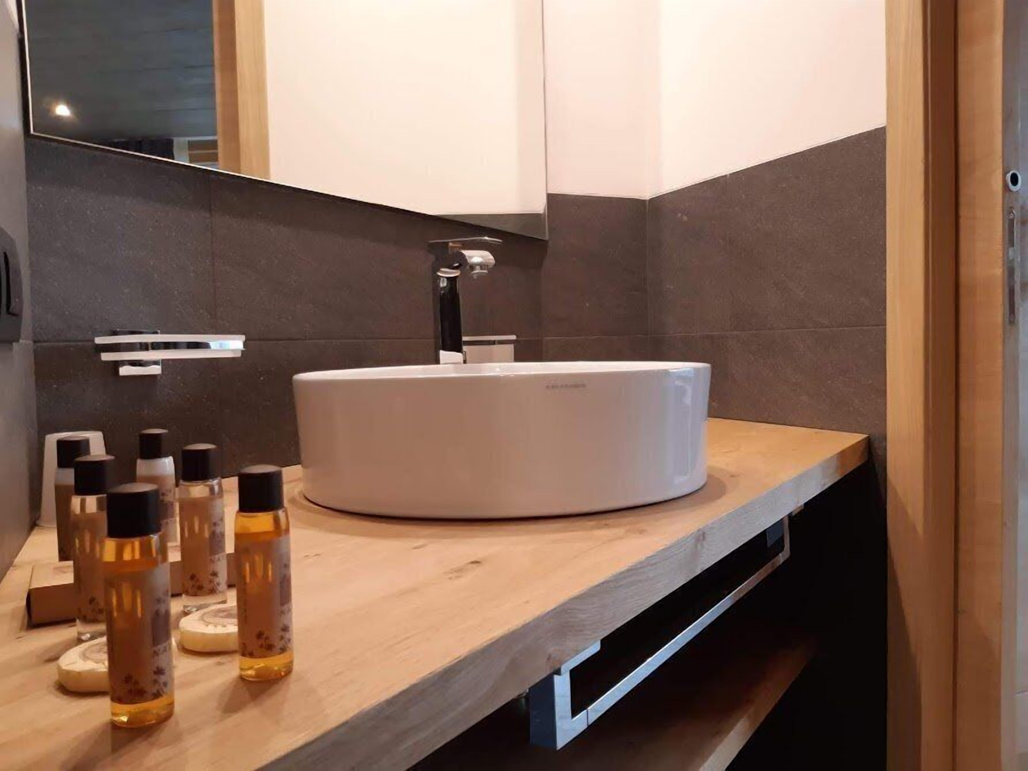 A modern bathroom with a round white sink, dark tiled walls, and a wooden countertop.