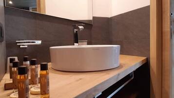 A modern bathroom with a round white sink, dark tiled walls, and a wooden countertop.