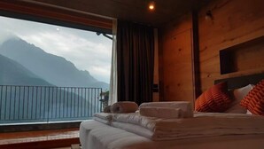 A bedroom with a large window overlooking mountains, a wooden interior, and a bed with pillows and a rolled towel.