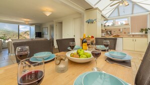 A dining area with a table set for two, featuring a bowl of fruit, wine glasses, and a bottle of wine.