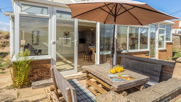 A covered patio area with a wooden table, a bench, and an umbrella.