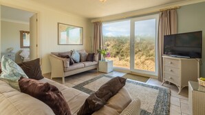 A spacious living room with a sofa, a television, and a large window offering a view of the outdoors.