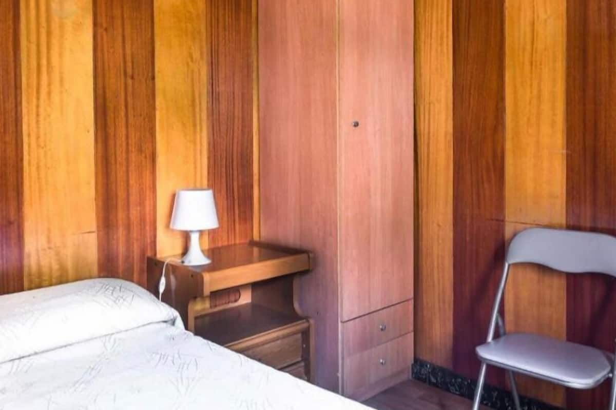 Una habitación con paneles de madera, una cama, un escritorio con lámpara y una silla.