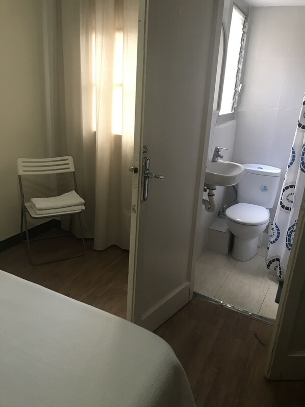 Una habitación con cama, una silla, y baño con inodoro, lavamanos y cortina de ducha.