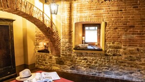 Una habitación acogedora con pared de piedra, puerta de madera, una ventana pequeña y colcha roja.
