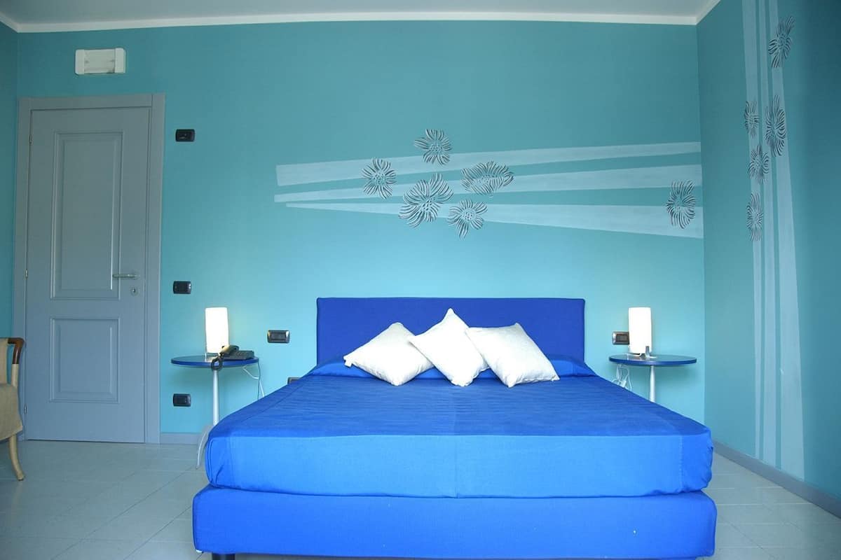 A bedroom with a blue bed, white pillows, two bedside tables with lamps, and a door.
