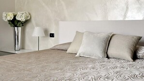 A bedroom with a patterned bedspread, a white headboard, and a vase with flowers on a bedside table.