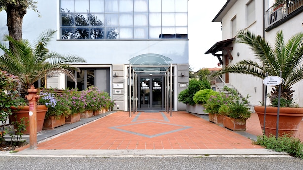 A hotel entrance with a glass canopy, potted plants, and a statue.