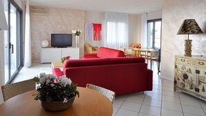 A modern living room with a red sofa, a television, a dining area with a table and chairs, and a decorative cabinet.
