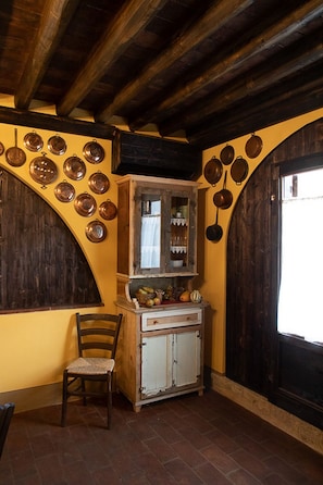Une cuisine rustique avec des poutres en bois, un buffet rempli de vaisselle et une chaise.
