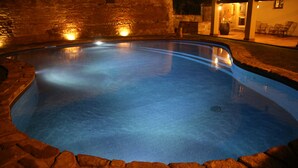 Una piscina con bordo in pietra, circondata da un muro in mattoni e un’area patio con sedie.