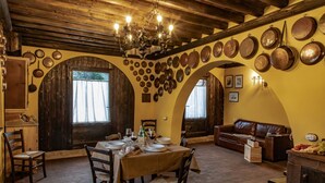 Zona pranzo con tavolo apparecchiato per quattro, circondato da sedie in legno. Diverse pentole sono appese alle pareti e un lampadario pende dal soffitto.