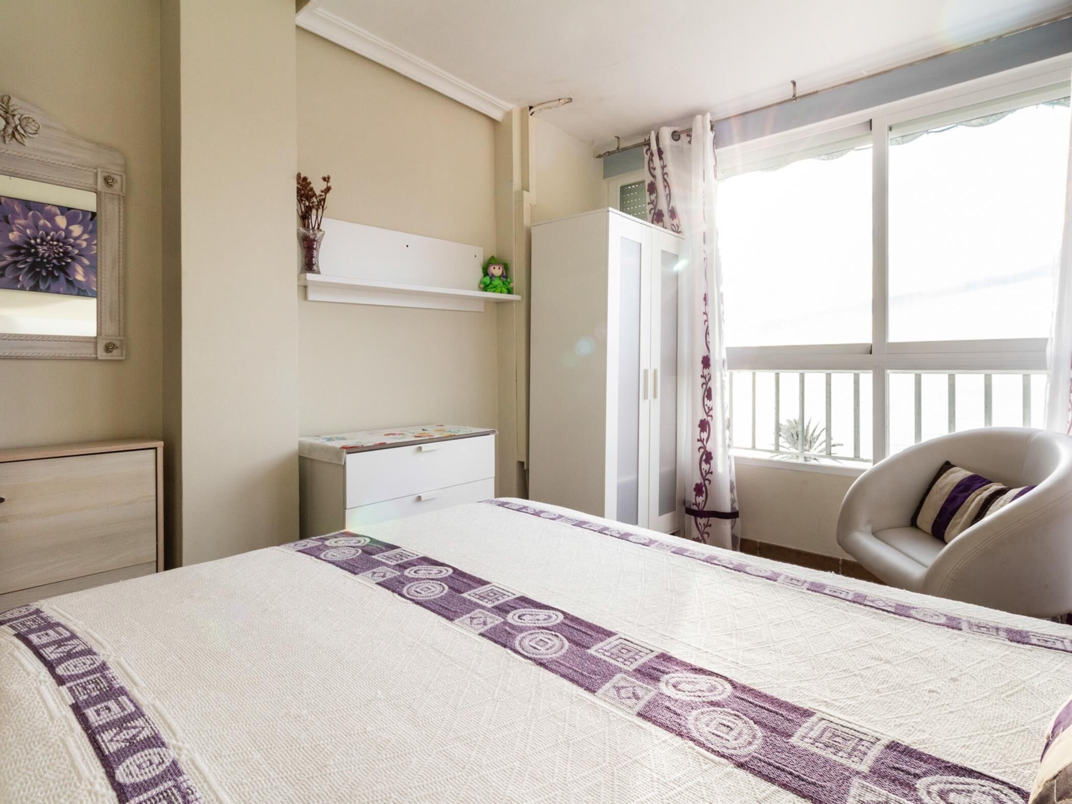 A bedroom with a bed, a dresser, a vanity, a chair, and a window with a view.
