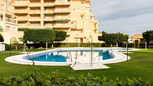 Une piscine entourée d’une pelouse bien entretenue, avec un immeuble à plusieurs étages en arrière-plan.