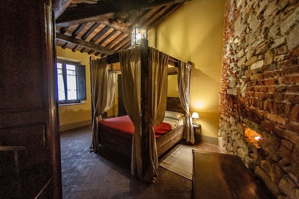 A rustic bedroom with a four-poster bed, stone walls, and a wooden ceiling.