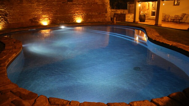 A swimming pool with a stone border, surrounded by a brick wall and a patio area with chairs. - Apt. LA TORRE - "Manor of Brunelleschi" Medieval Apartments Resort (Vicopisano)