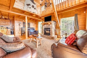 L'intérieur d'un chalet en bois, avec une cheminée en pierre, des meubles en cuir et un téléviseur.