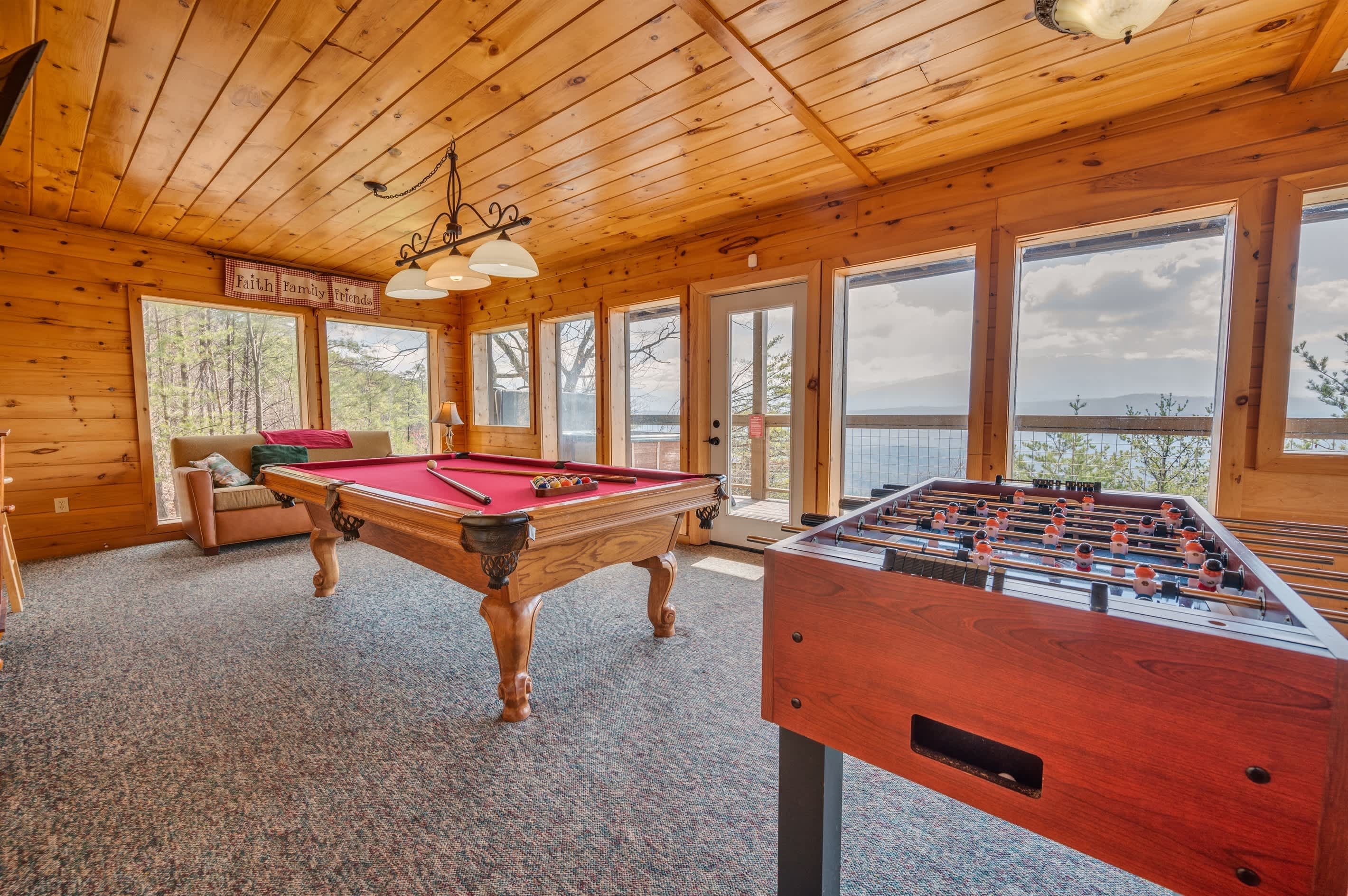 A wooden interior with a pool table, foosball table, and a sofa.