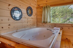 A wooden cabin interior with a large bathtub, two ornate mirrors, and a window with curtains.