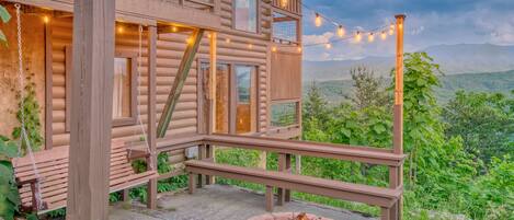 Une cabane en bois dotée d’une terrasse, d’un foyer et de guirlandes lumineuses.