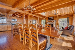 Interior de uma cabana de madeira com área de jantar, cozinha e espaço para sentar.