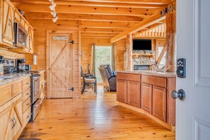 L’intérieur d’une cabane avec des murs en bois, un coin cuisine, un espace repas et une cheminée.