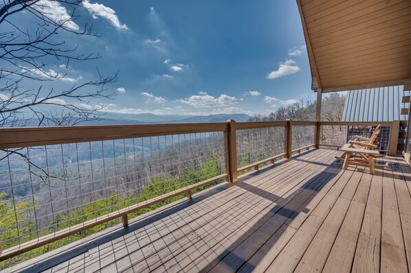 Une terrasse en bois avec une rambarde en métal, d’où l’on peut admirer un paysage montagneux.